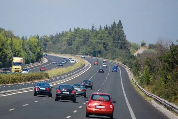 Carros e caminhão em viagem por uma rodovia duplicada cercada de árvores